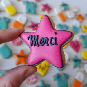 Close-up of a pink star-shaped cookie with 'Merci' icing amidst a variety of colorful cookies.